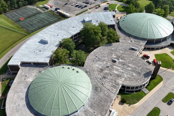 Aerial view of a large building complex with green domed roofs and surrounding parking lots.