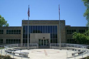 Modern building with a circular plaza, flagpoles, and curved metal railing under a clear blue sky
