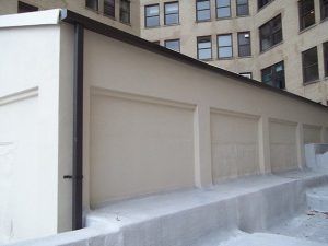 Beige rooftop utility structure with closed panels beside a stone office building
