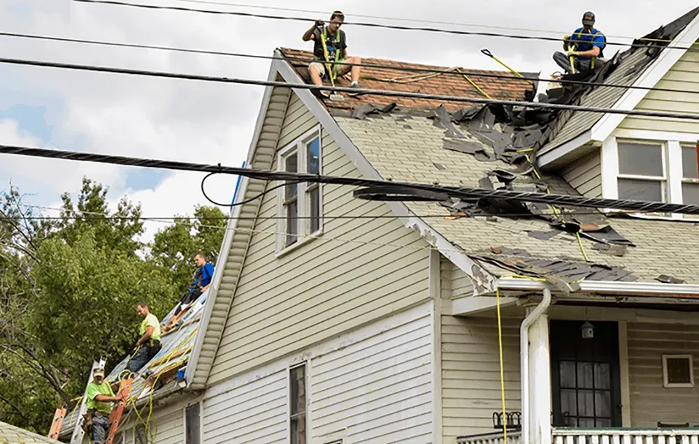Workers repairing storm-damaged roof on a house, with ladders and shingles removed