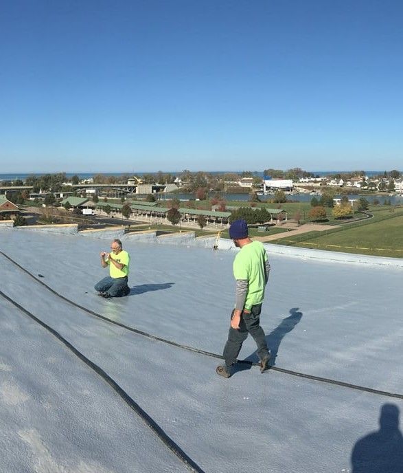 Two workers in neon safety shirts on a flat rooftop with a city view in the background.