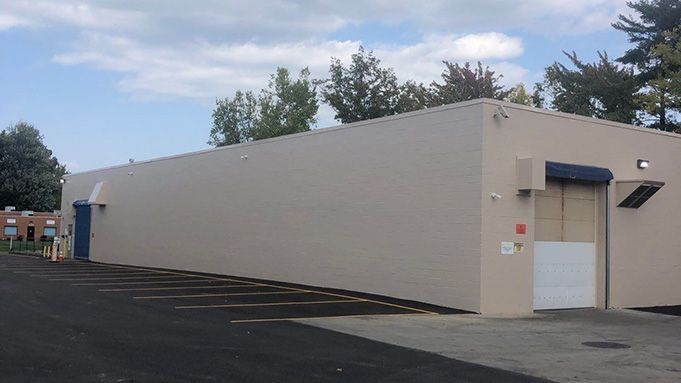 Long beige industrial building with a garage door and blue awning in a parking lot