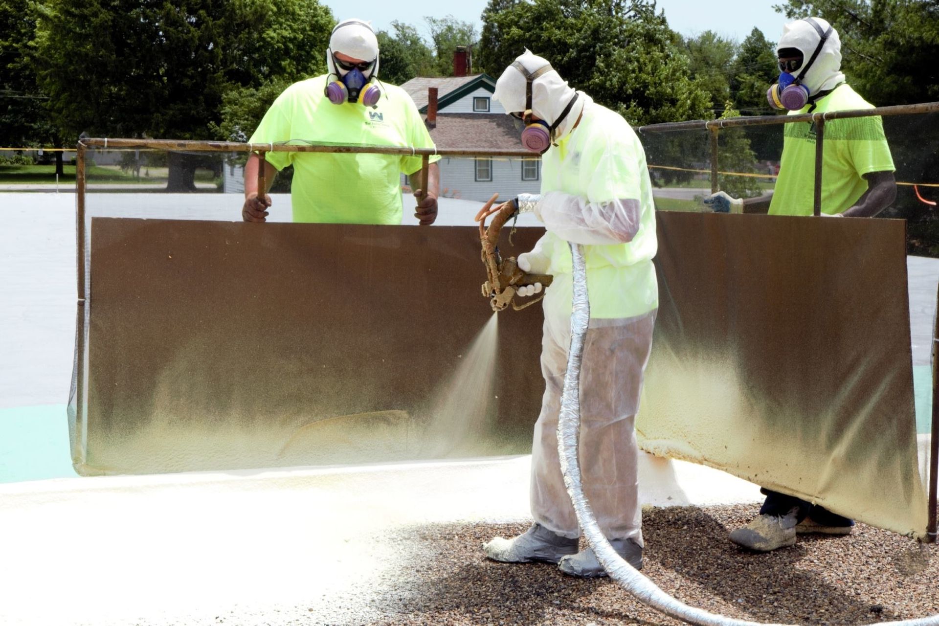 Workers in protective gear spray-painting a large metal surface outdoors
