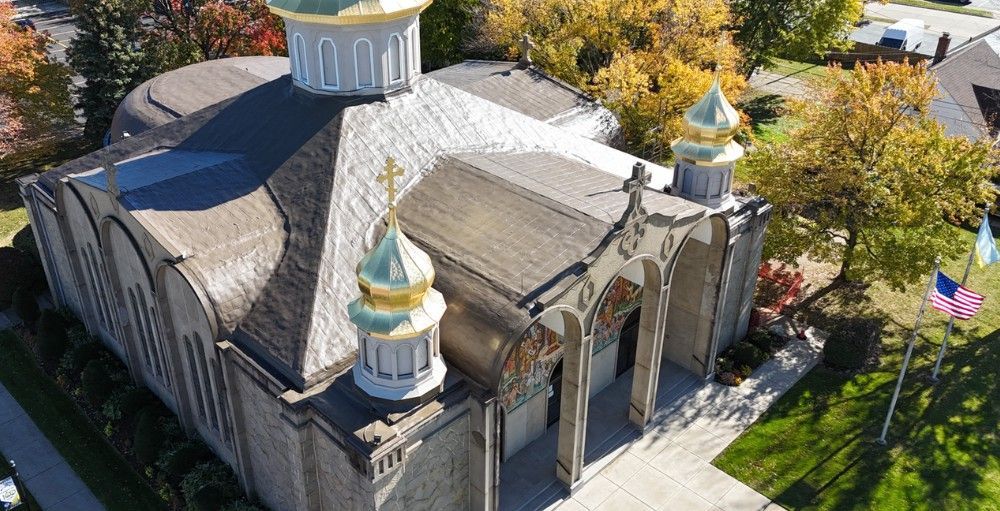 Aerial view of a stone church with domes, surrounded by autumn trees and a lawn.