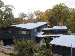 Modern dark-gray houses with light roofs nestled among autumn trees on a wooded hillside
