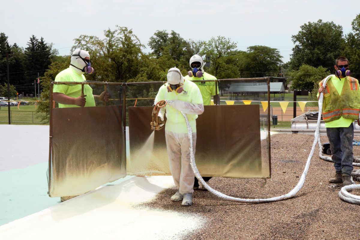 Workers in protective gear spraying a white coating on a barrier outdoors