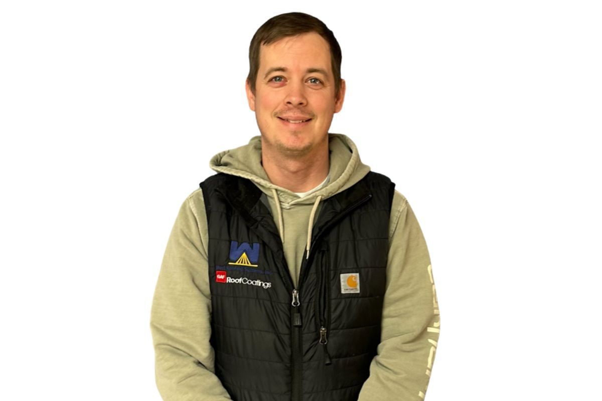 Smiling person in a green hoodie and black vest, seated against a plain white background.