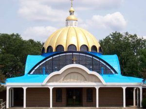 Golden-domed temple with blue roof and arched entrance, framed by trees under a cloudy sky