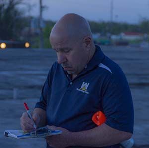 Man in blue jacket writing on a notepad outdoors at dusk
