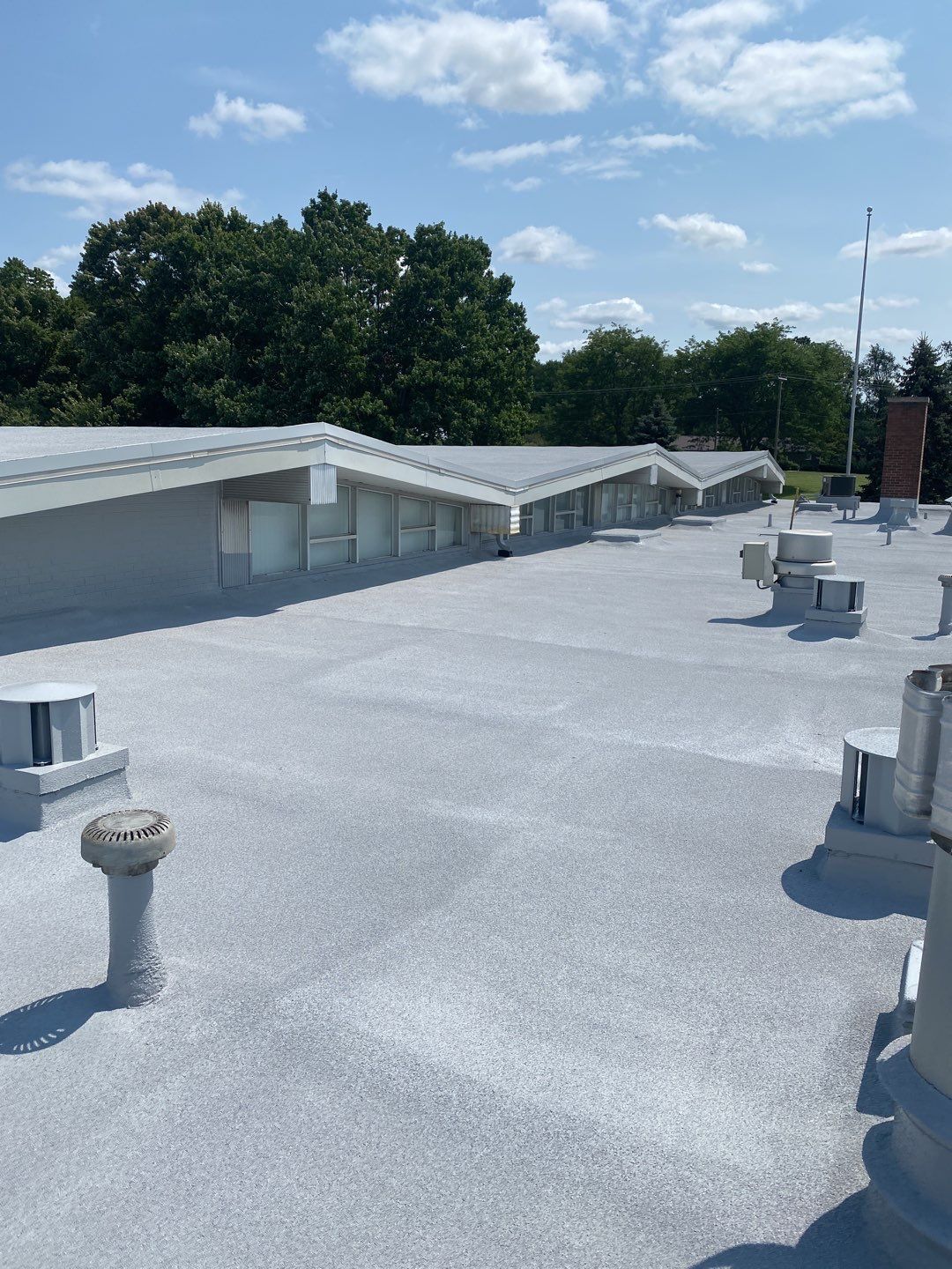 Rooftop with gray gravel surface, vents, skylights, and trees under a blue sky
