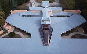 Aerial view of a futuristic modern building with a geometric gray roof and central glass entrance.
