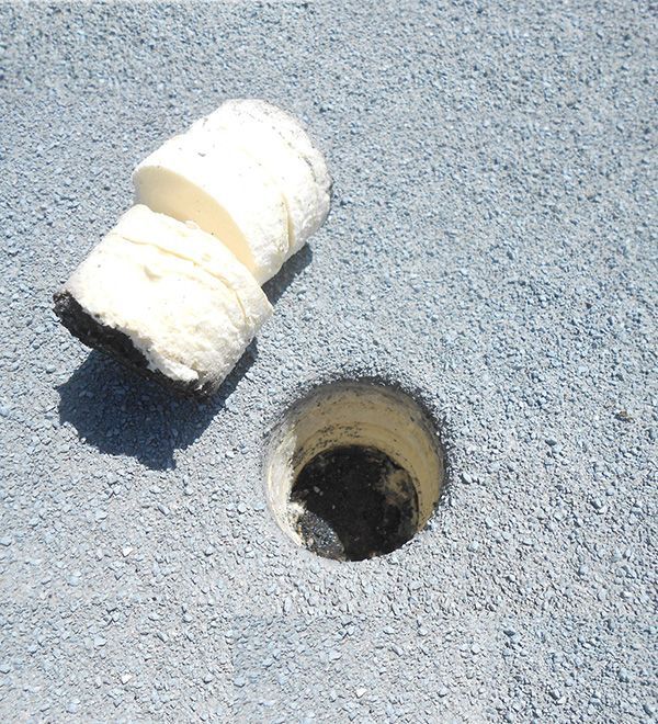 Broken white foam piece beside a small round hole in gray pavement