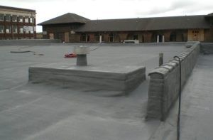 Flat rooftop with gray membrane, low parapet walls, and a brick building in the background.