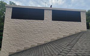 Exterior wall with two black vent openings above a sloped shingled roof.