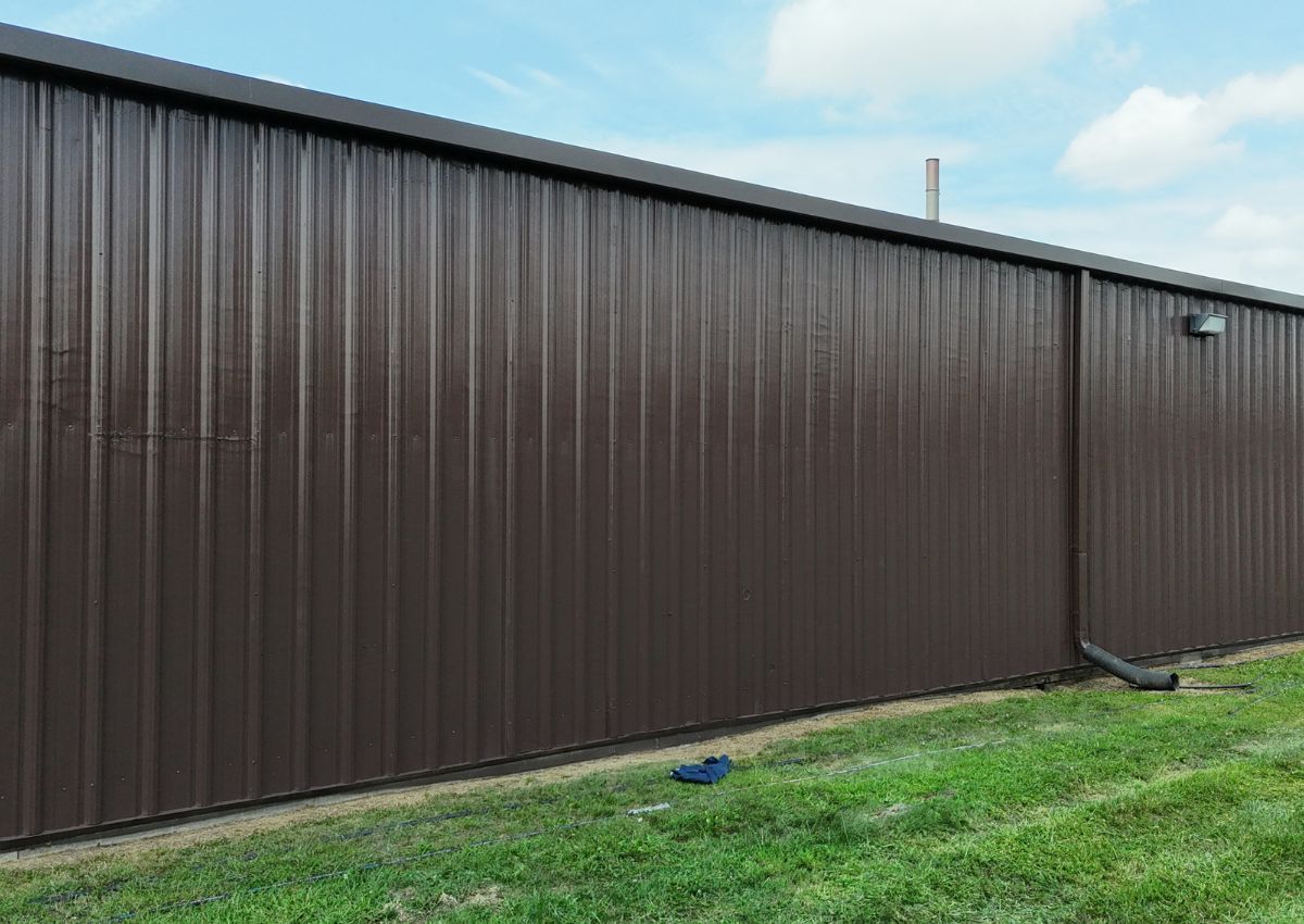 Brown metal building wall beside green grass under a cloudy sky