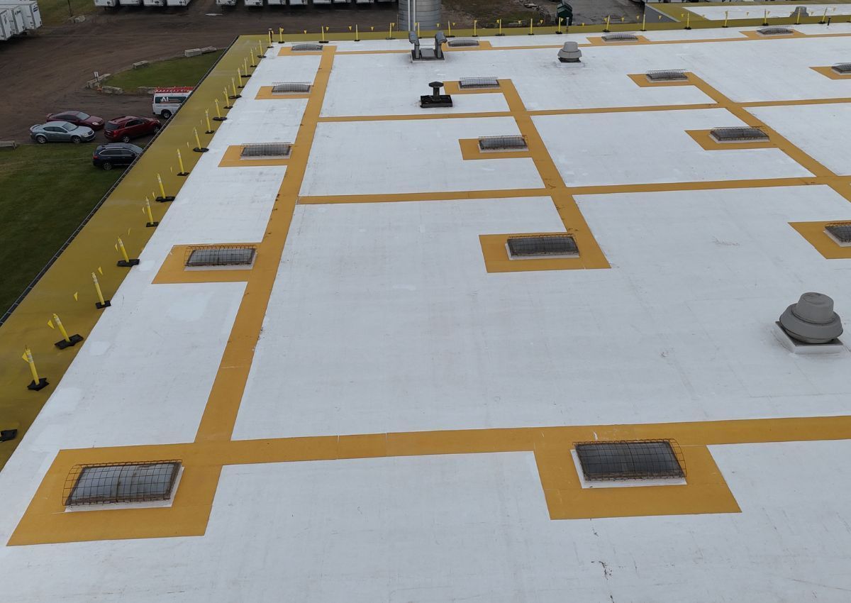 Flat white rooftop with yellow walkway lines and several vents and skylights.