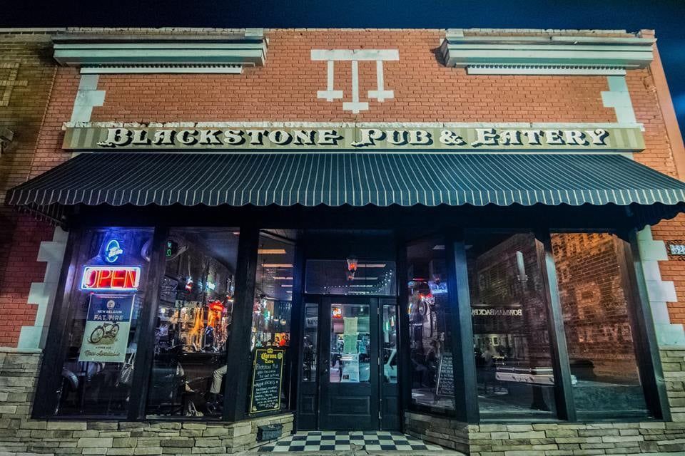 Blackstone Pub & Eatery storefront at night with lit windows, brick facade, and striped awning
