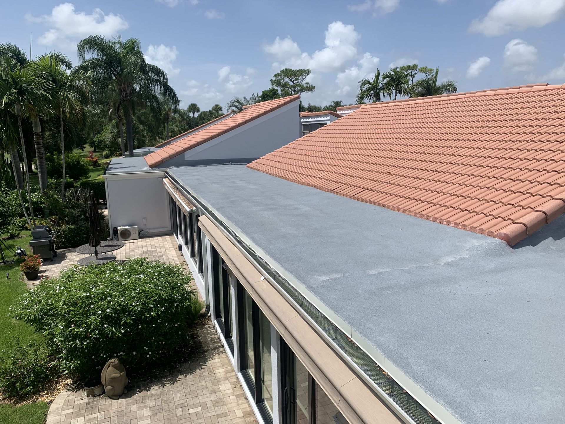 Aerial view of a building with red tile roof, gray rooftop, and palm trees nearby.