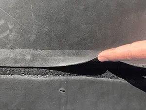 Finger lifting a torn black fabric edge, exposing the frayed seam underneath