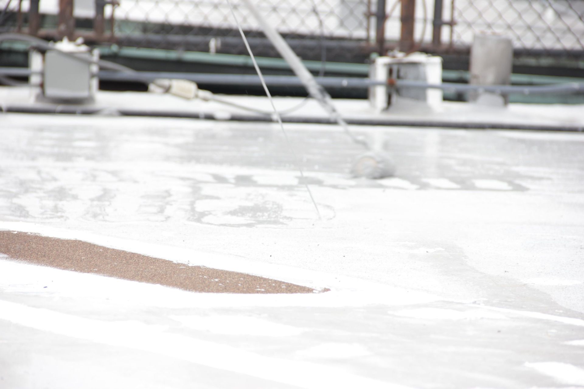 Rainwater streaming across a white rooftop with a brown strip and blurred railings in the background