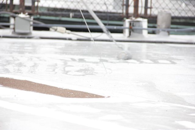 Rainwater streaming across a white rooftop with a brown strip and blurred railings in the background