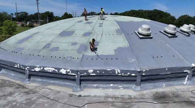 Flat industrial rooftop with workers and several white vents under a bright sky.