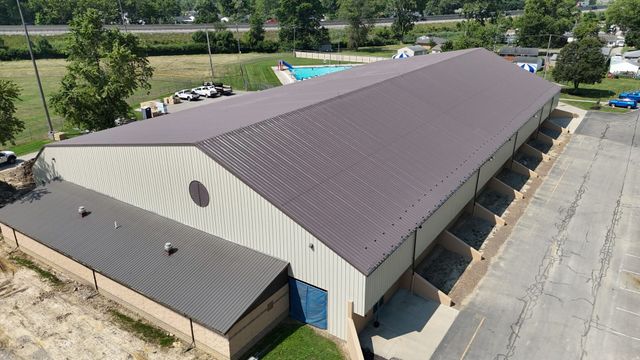Aerial view of a large tan warehouse with a brown roof and loading docks beside an empty parking lot.
