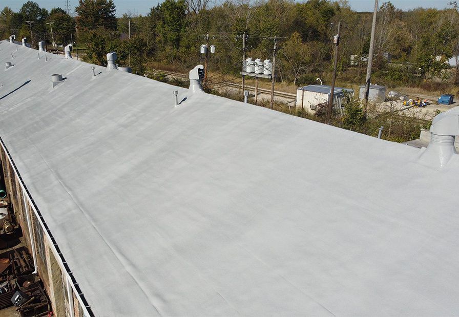Large white rooftop with several vents, seen from above with trees in the background