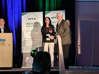 Award ceremony on stage with a man presenting a plaque to a woman beside SPFA Industry Excellence banners