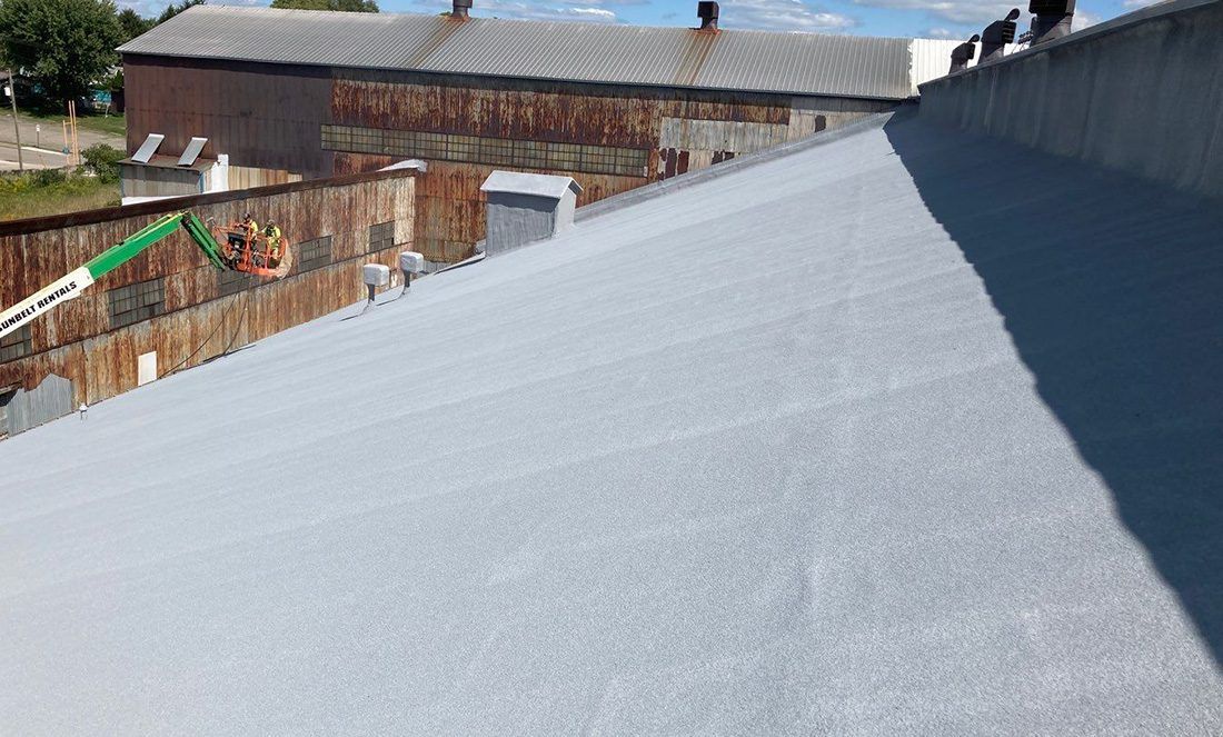 Blue-gray sloped roof under construction beside buildings on a sunny day
