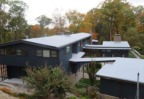 Modern dark-gray house with a silver roof surrounded by autumn trees