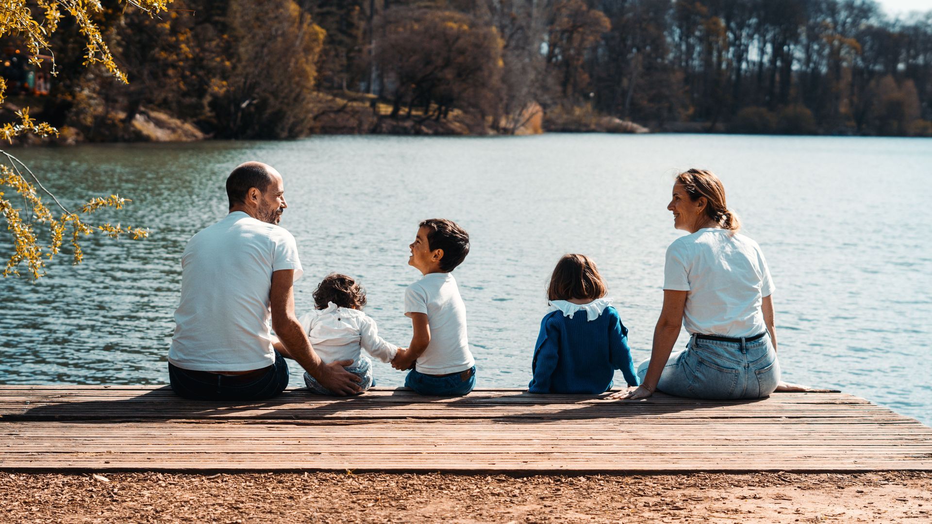 Family standing outside a wooden cabin with pine trees and mountains in the background.