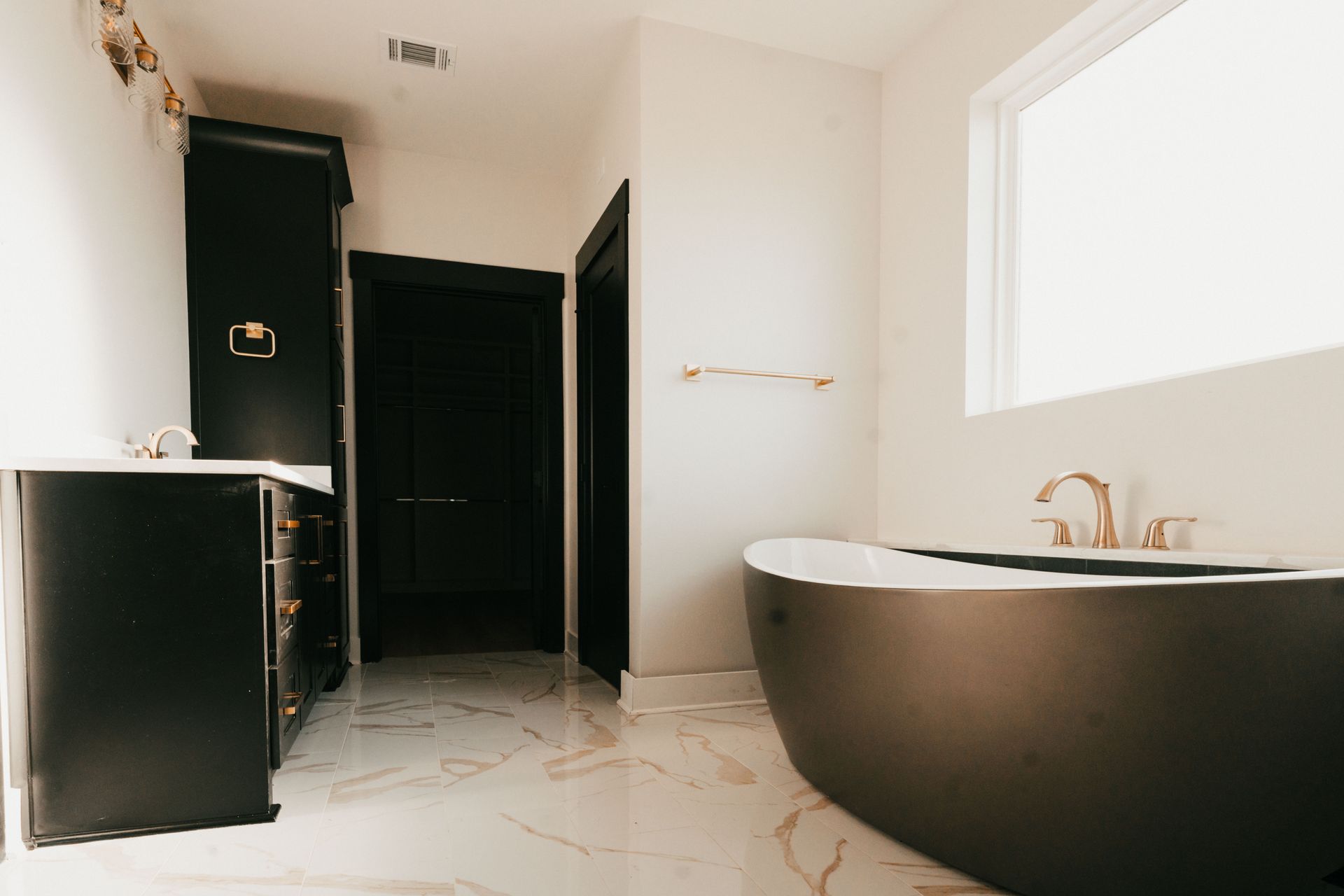 Bathroom with black bathtub, black cabinetry, and modern marble flooring.