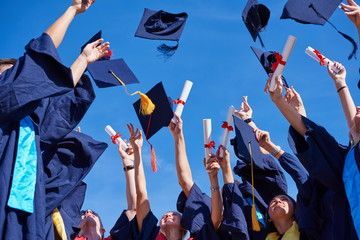 Graduates in blue gowns and mortarboards toss caps and diplomas into the air.