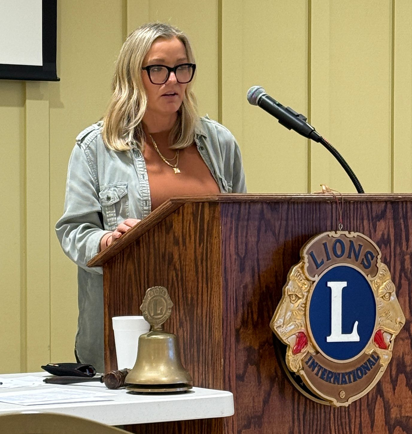 Woman speaking at a Lions Club podium, microphone in front.