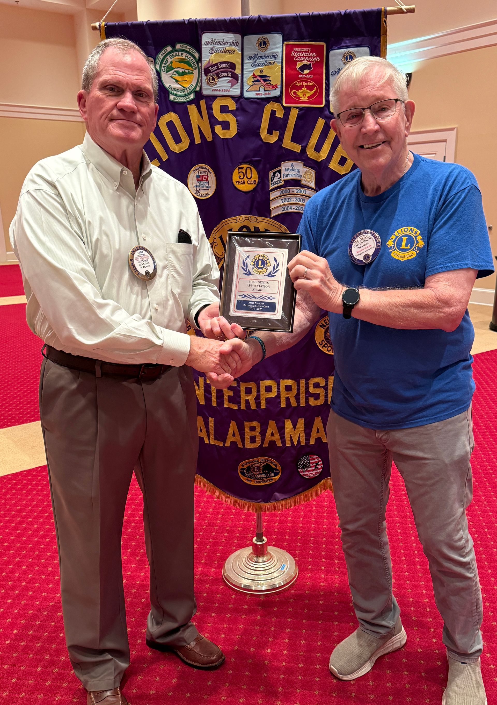 Two men holding an award in front of a Lions Club banner, Enterprise, Alabama.