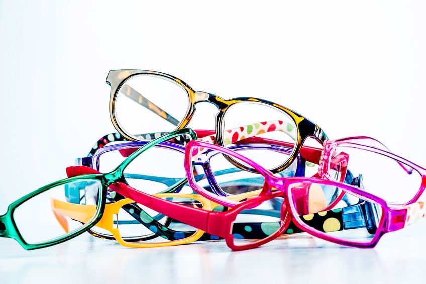 Pile of colorful eyeglasses on a white surface, frames in various bright colors and patterns.