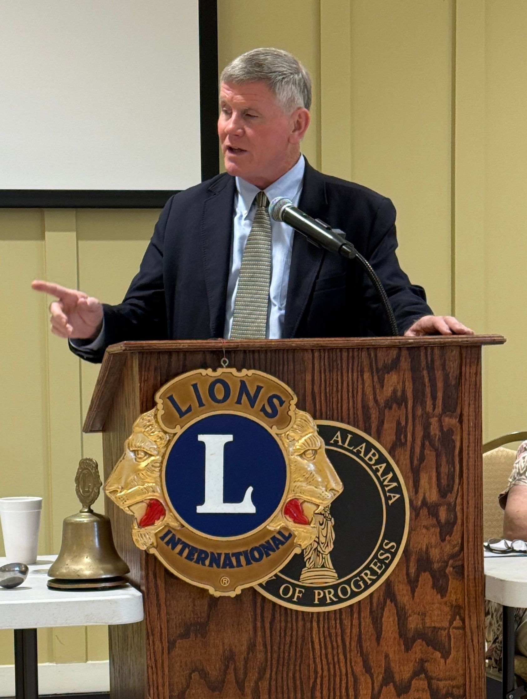 Man speaking at a Lions Club podium, gesturing during a meeting