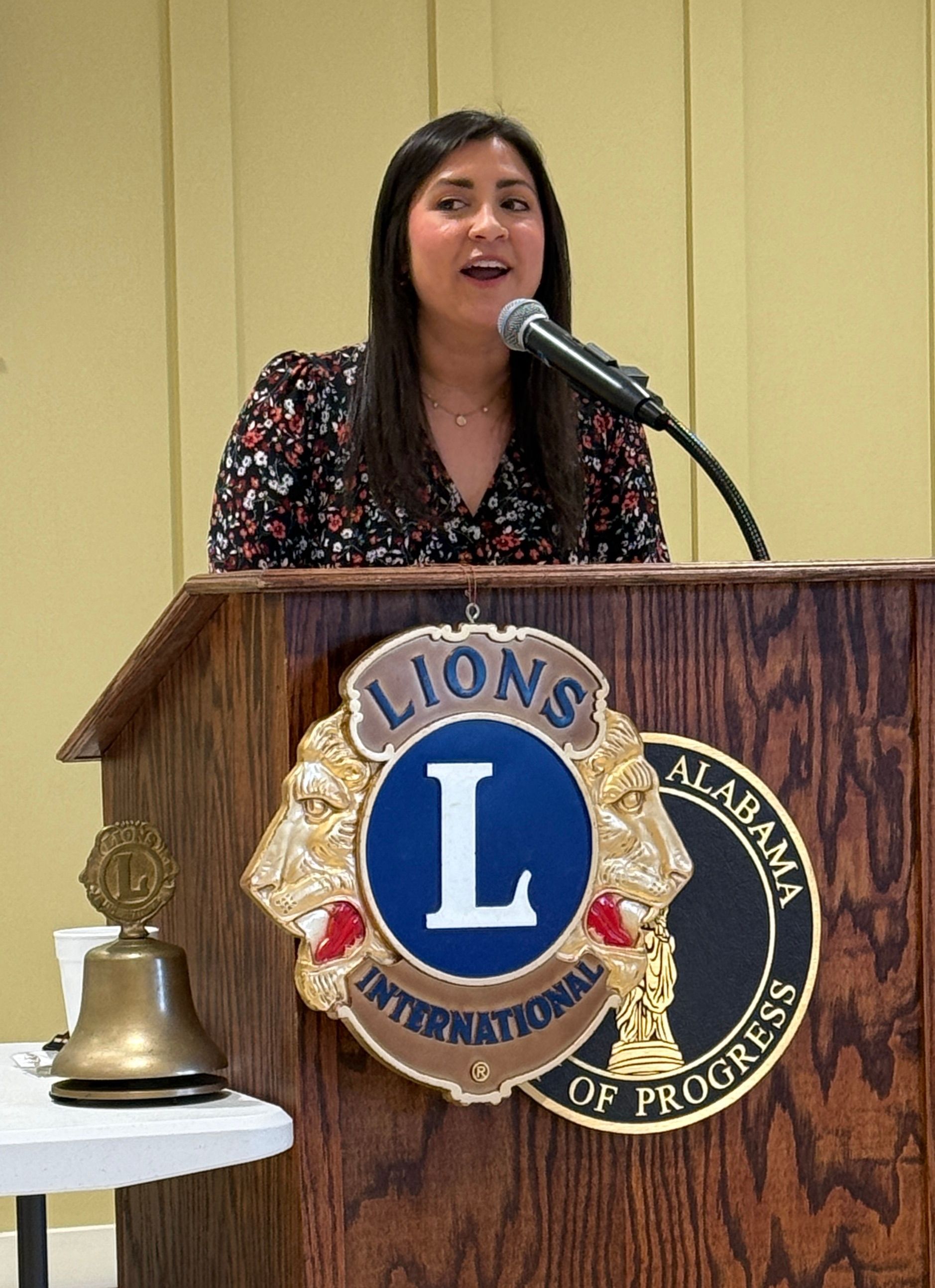 Woman speaking at a podium with a Lions International emblem in a meeting room