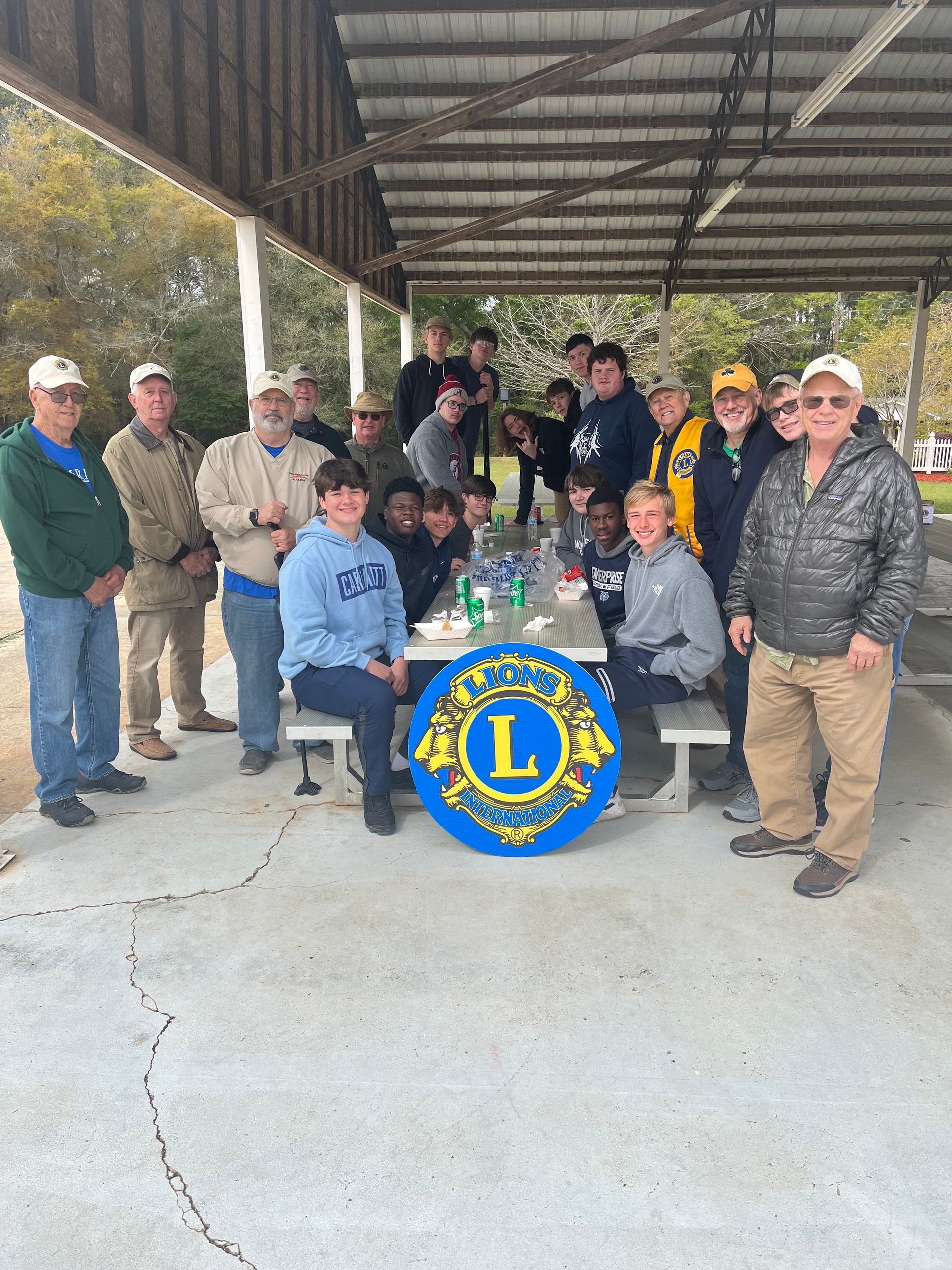 Group of people at a Lions Club event, gathered around a table under a shelter.
