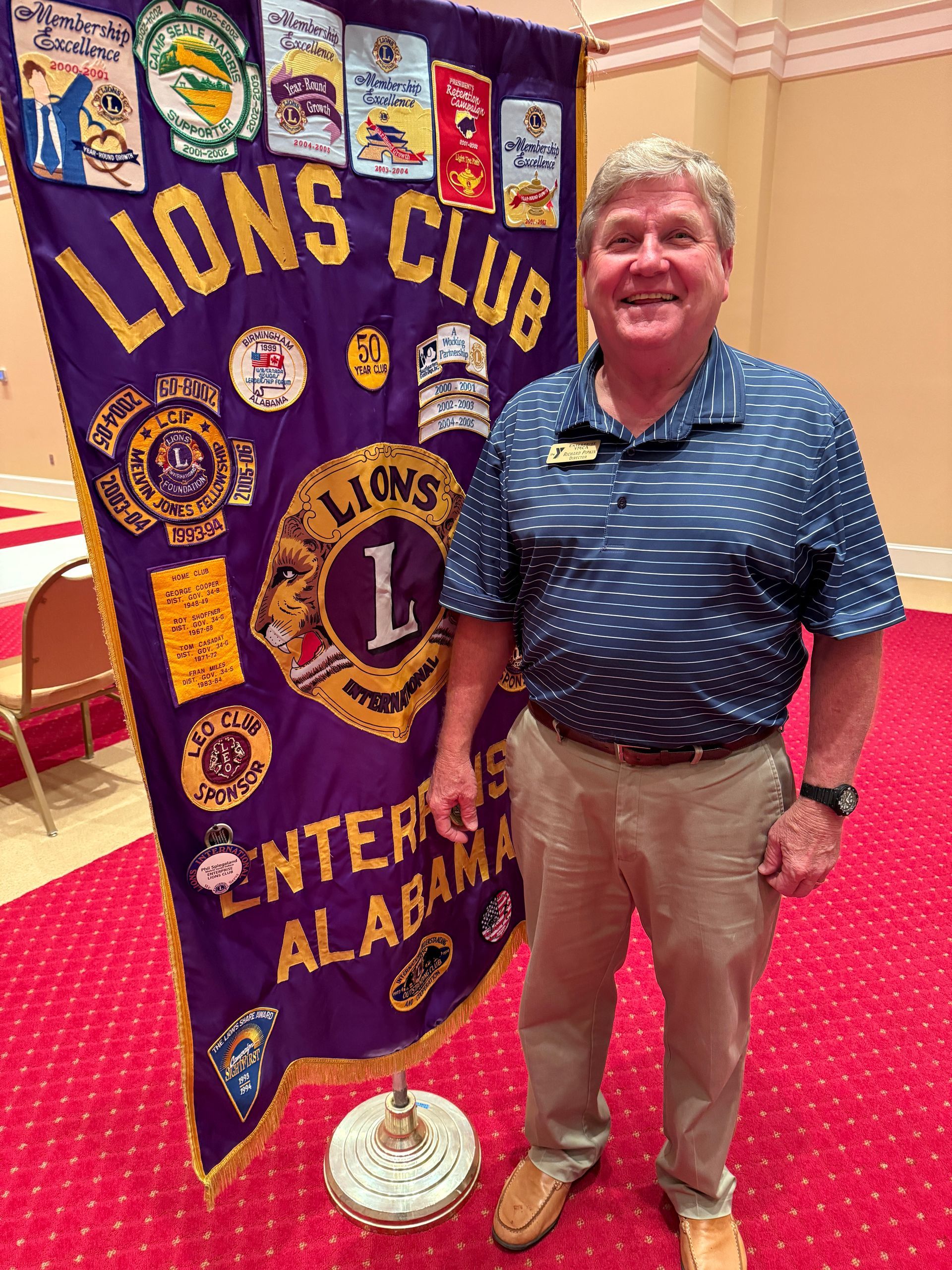 Man in blue shirt and khakis standing next to Lions Club banner, Enterprise, Alabama.