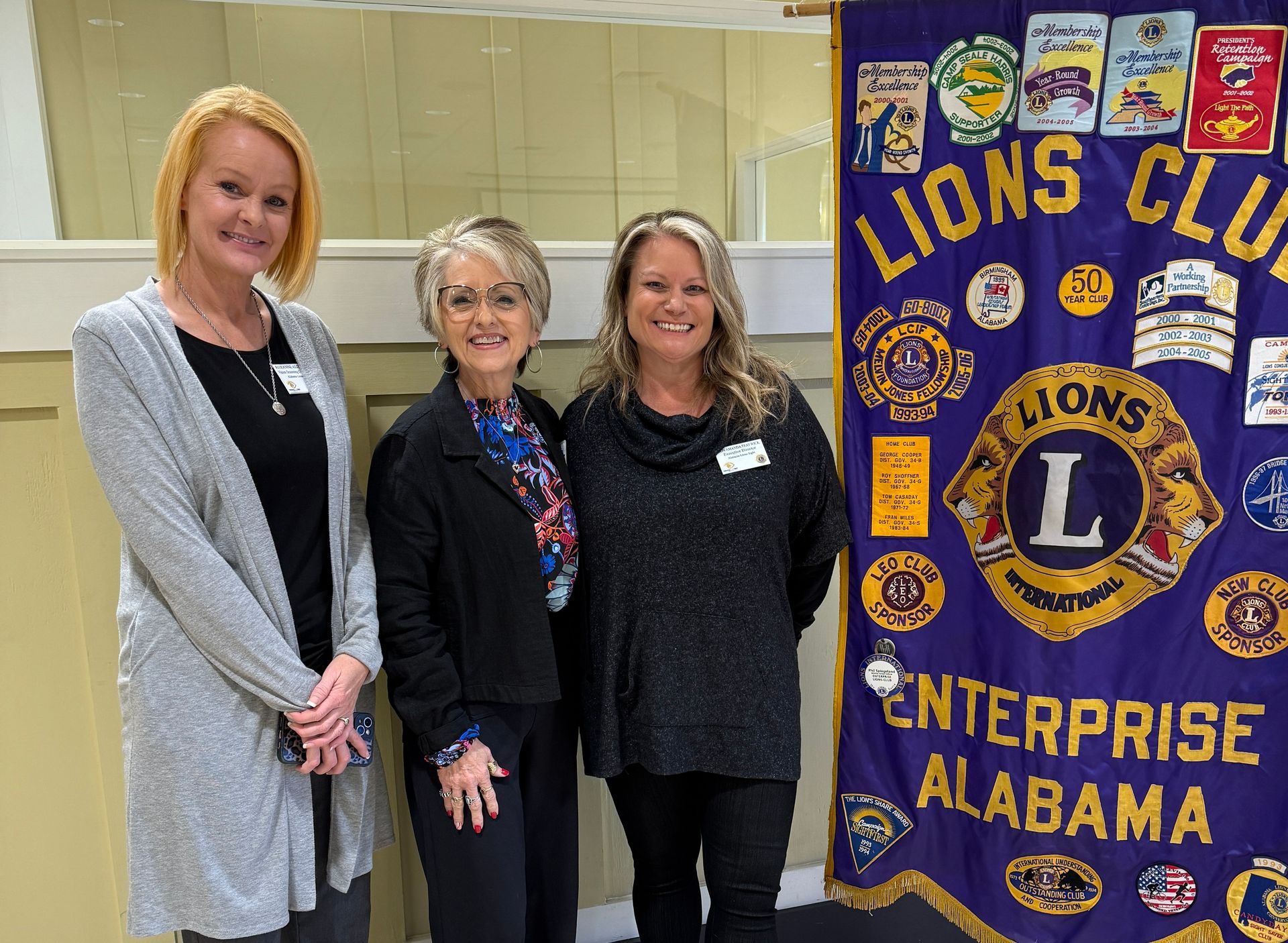 Three women standing next to a Lions Club banner. They are smiling.
