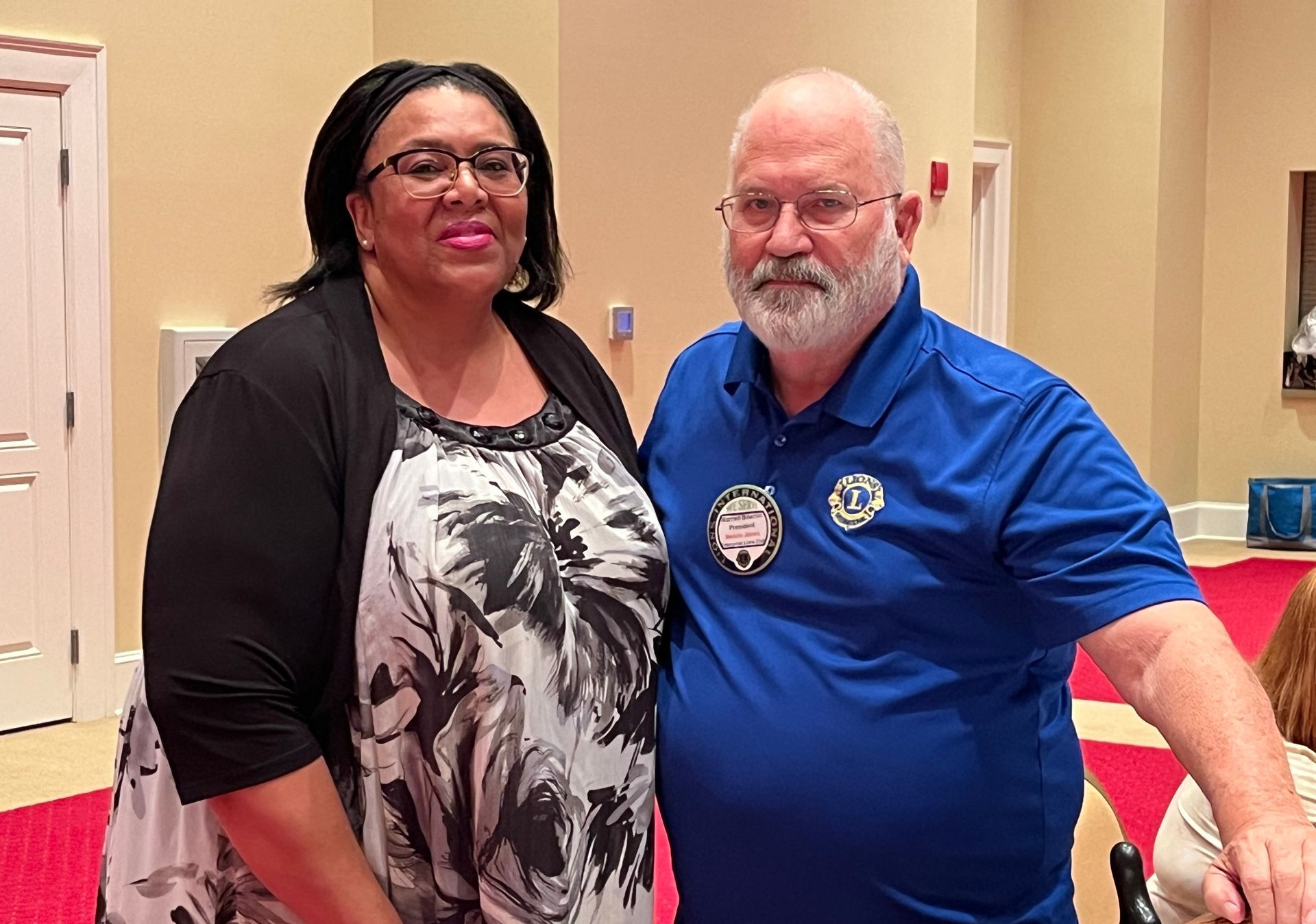 Woman in black/white dress and man in blue polo shirt standing together.