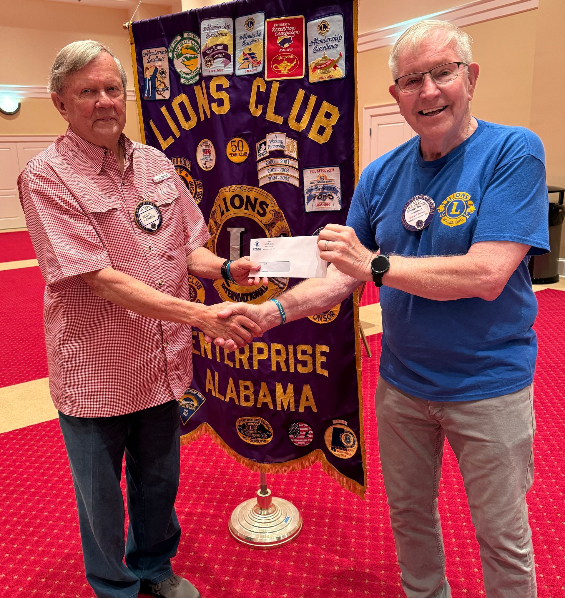 Two men shaking hands, one presenting a check in front of a 