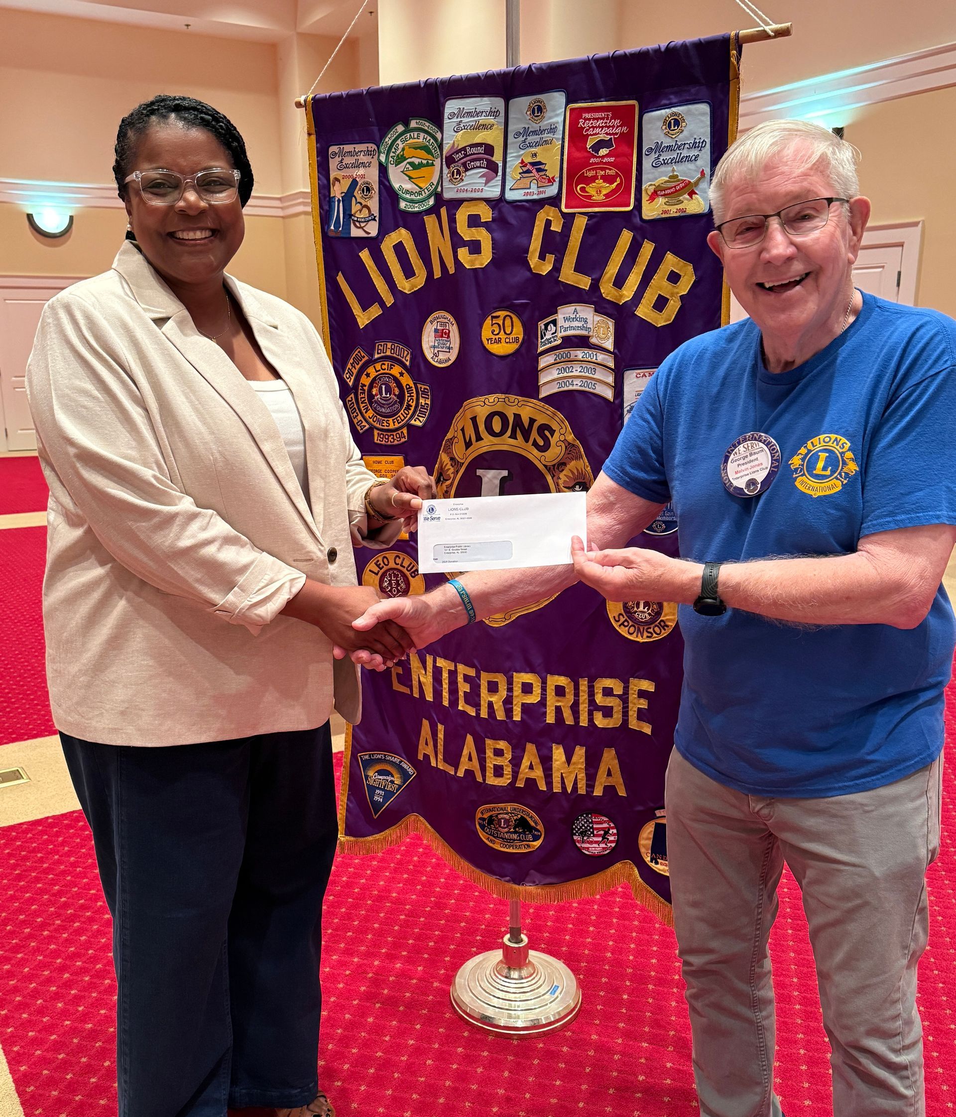 Woman and man exchanging a check in front of a Lions Club banner in Enterprise, Alabama.