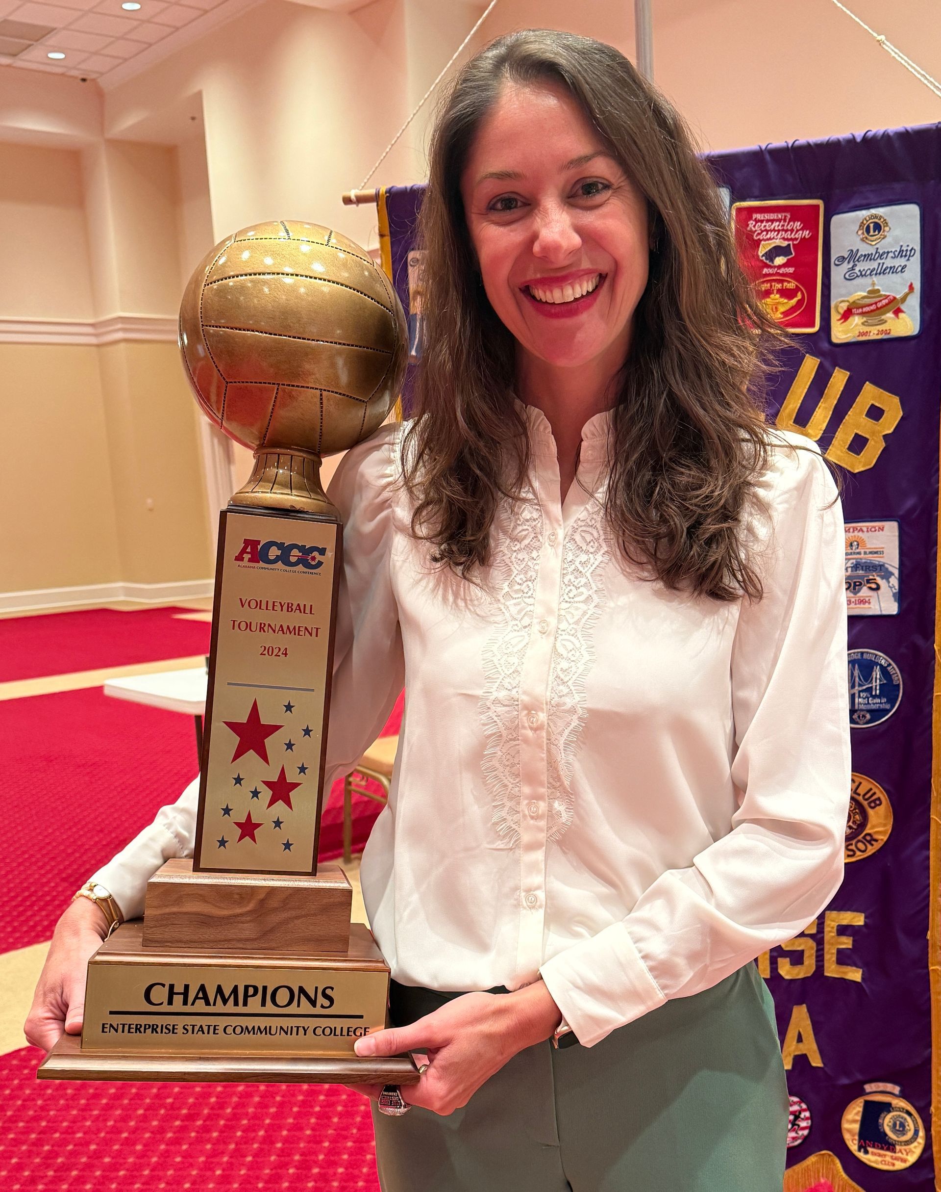 Woman smiles, holding a trophy that reads 