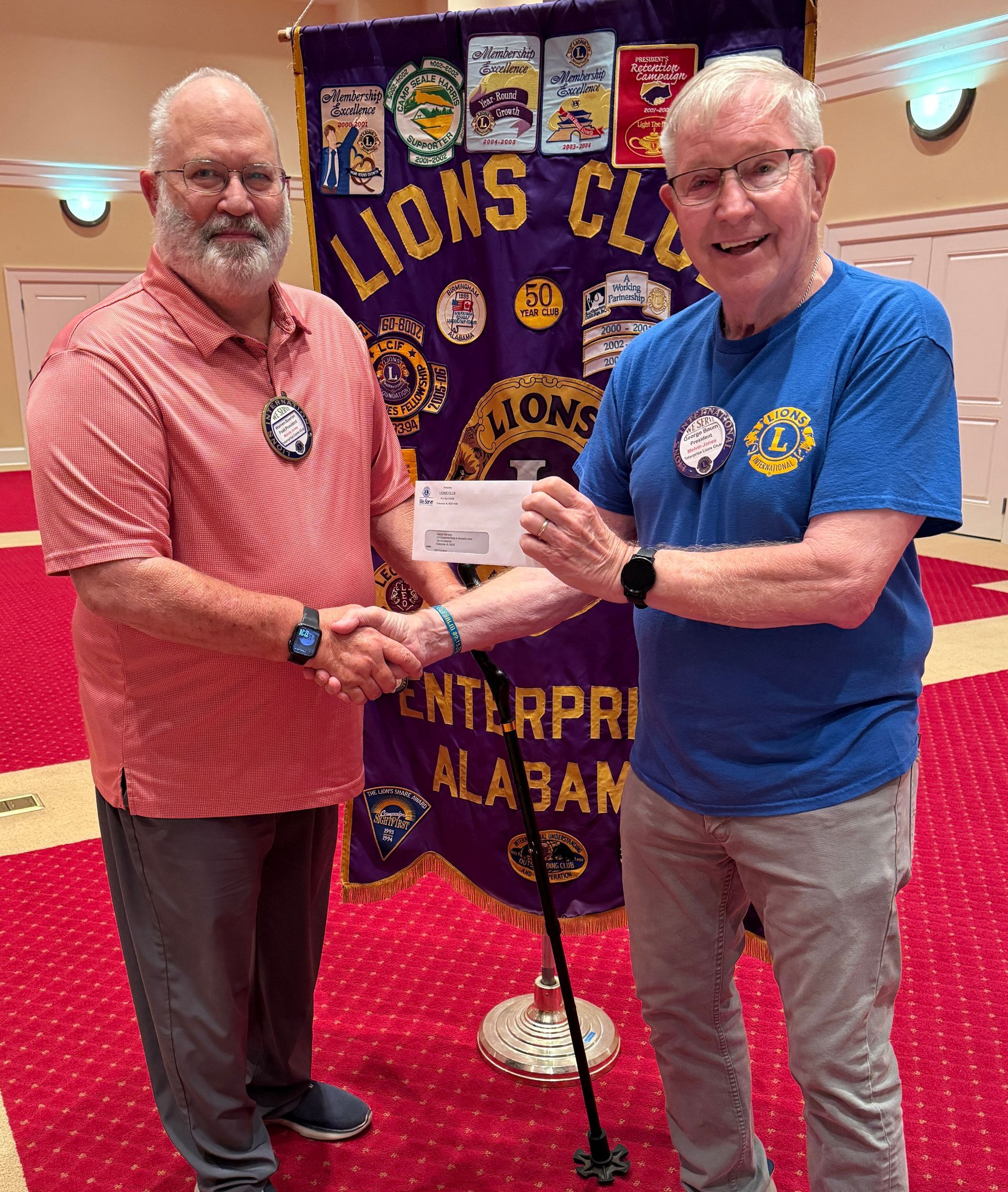 Two men shaking hands in front of a Lions Club banner. One hands over a check.