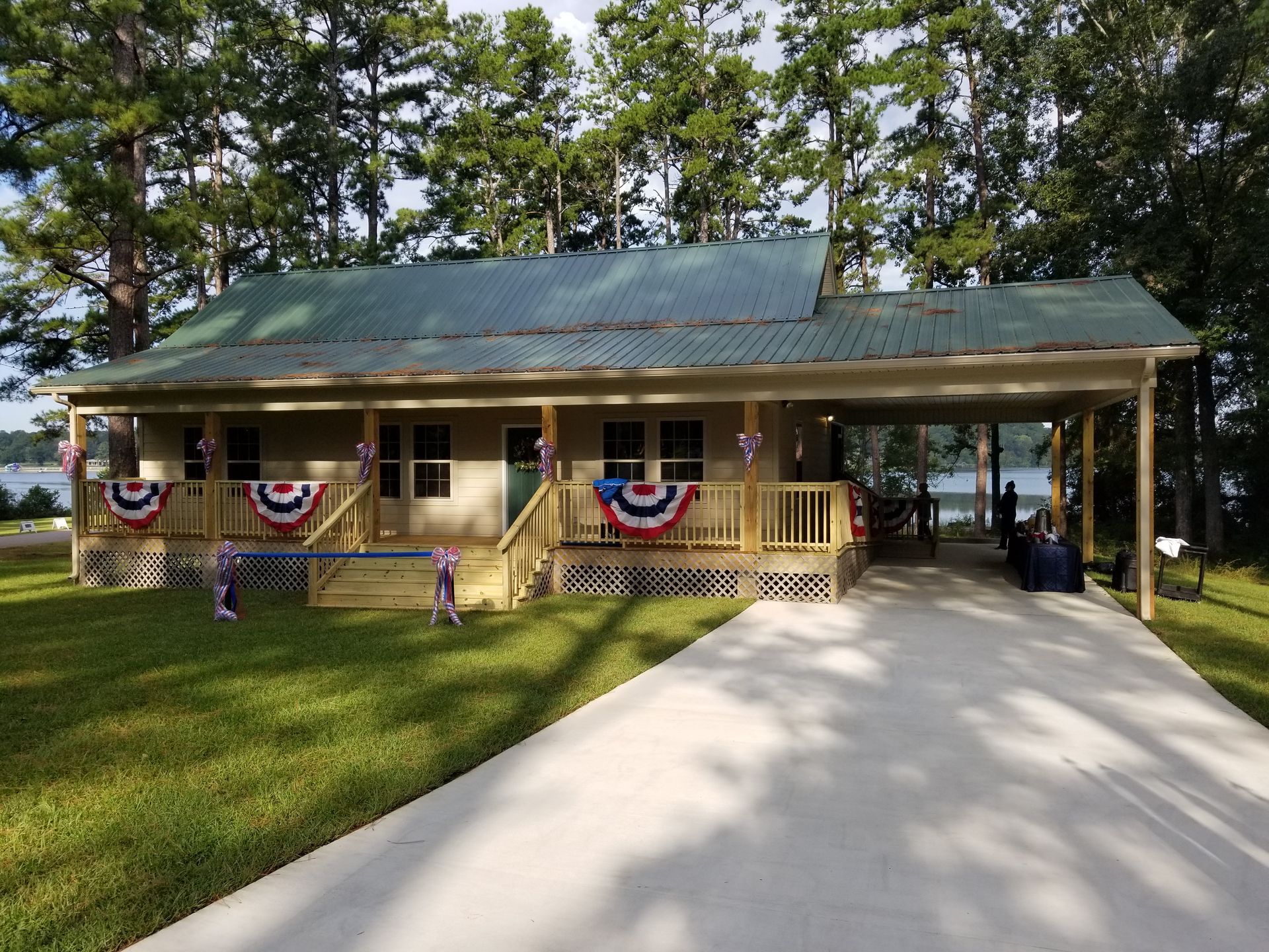 Cottage with carport decorated with patriotic bunting, overlooking a lake, on a sunny day.