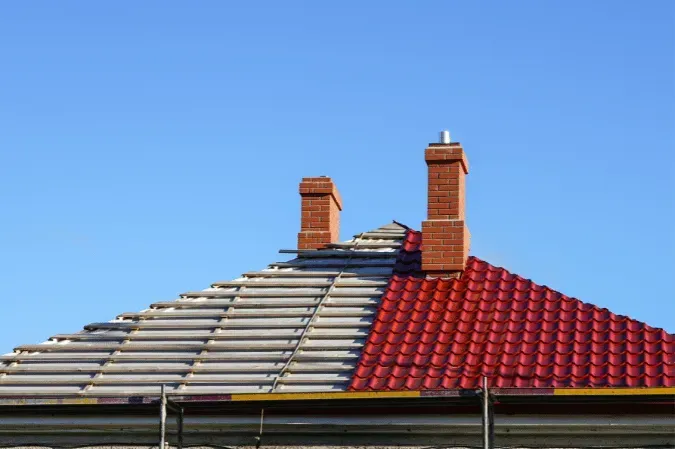 Row of suburban rooftops with red and gray tiles and two brick chimneys under a clear blue sky
