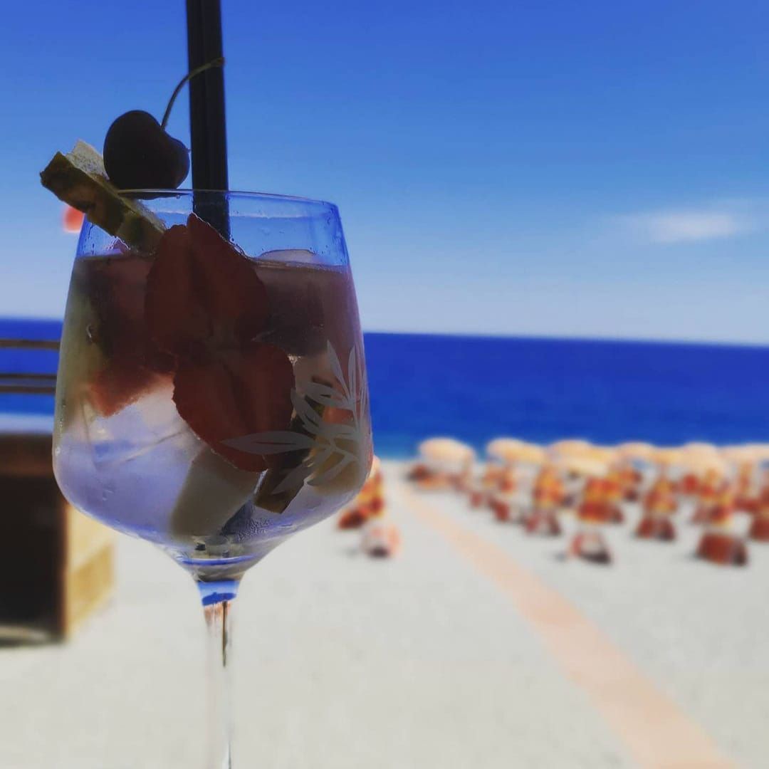 Un bicchiere di vino con una cannuccia dentro è su una spiaggia.